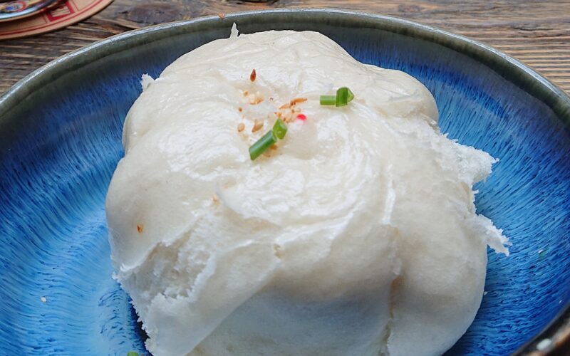 Chinesische Baozi: Eine gefüllte Teigtasche aus Hefetig auf blauem Teller.