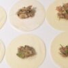 Teigtaschen füllen: Sechs Dumpling-Wrapper liegen auf hellem Hintergrund. Sie sind jeweils mit einer japanischen Garnelen-Gemüse-Mischung belegt und bereit, um gefaltet zu werden.