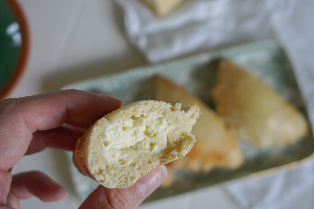 Eine angeschnittene bolivianische Empanada mit Käsefüllung. Im Hintergrund sind unscharf vollständige Empanadas zu sehen